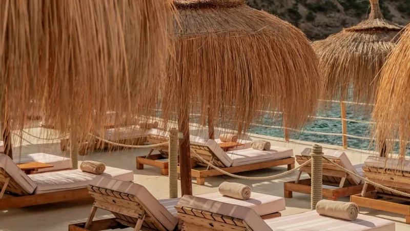 Straw parasols and wooden sunbeds above the water at Gran Folies